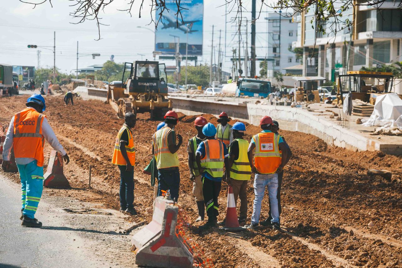 pexels-photo-35340757 Construction workers wearing safety gear at a busy roadwork site during the day.